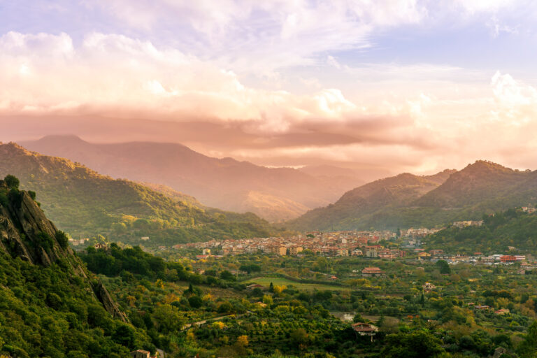 amazing sunset or sunrise in a mountain valley among slopes and hills with picturesque town on a rocky plato and nice cloudy sunset on background